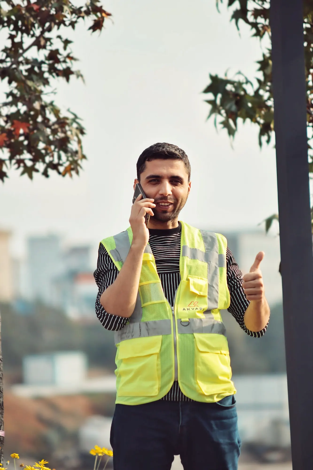 Smiling construction contractor in a hi-vis vest on a phone call giving a thumbs up
