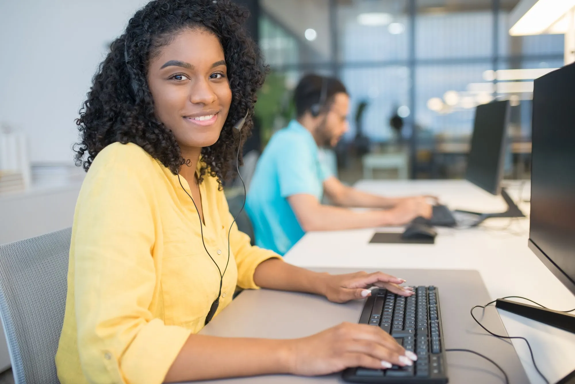 Smiling woman wearing a headset at her desk in a bright open office