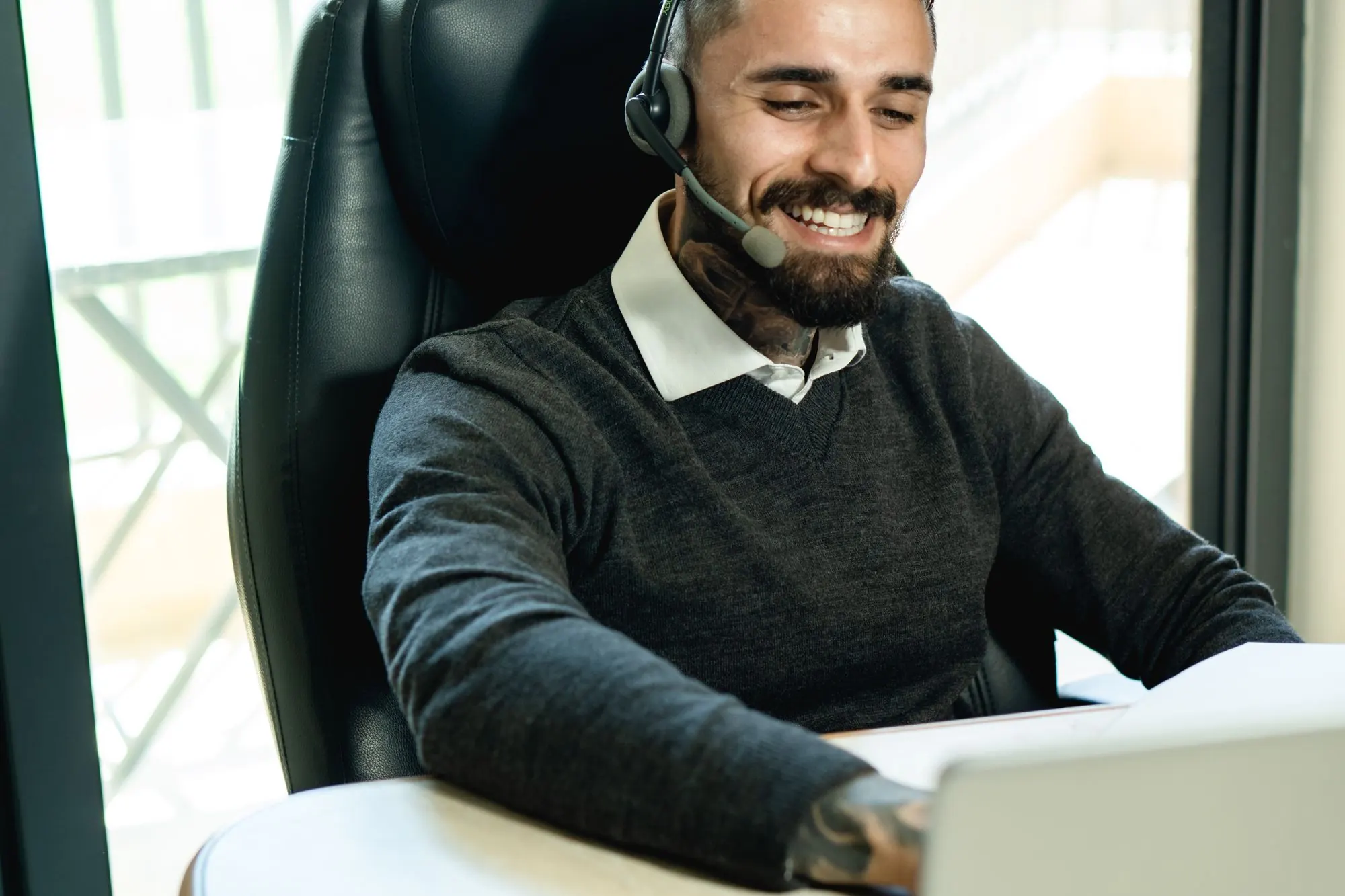 Smiling man on a headset call working at a laptop by a window