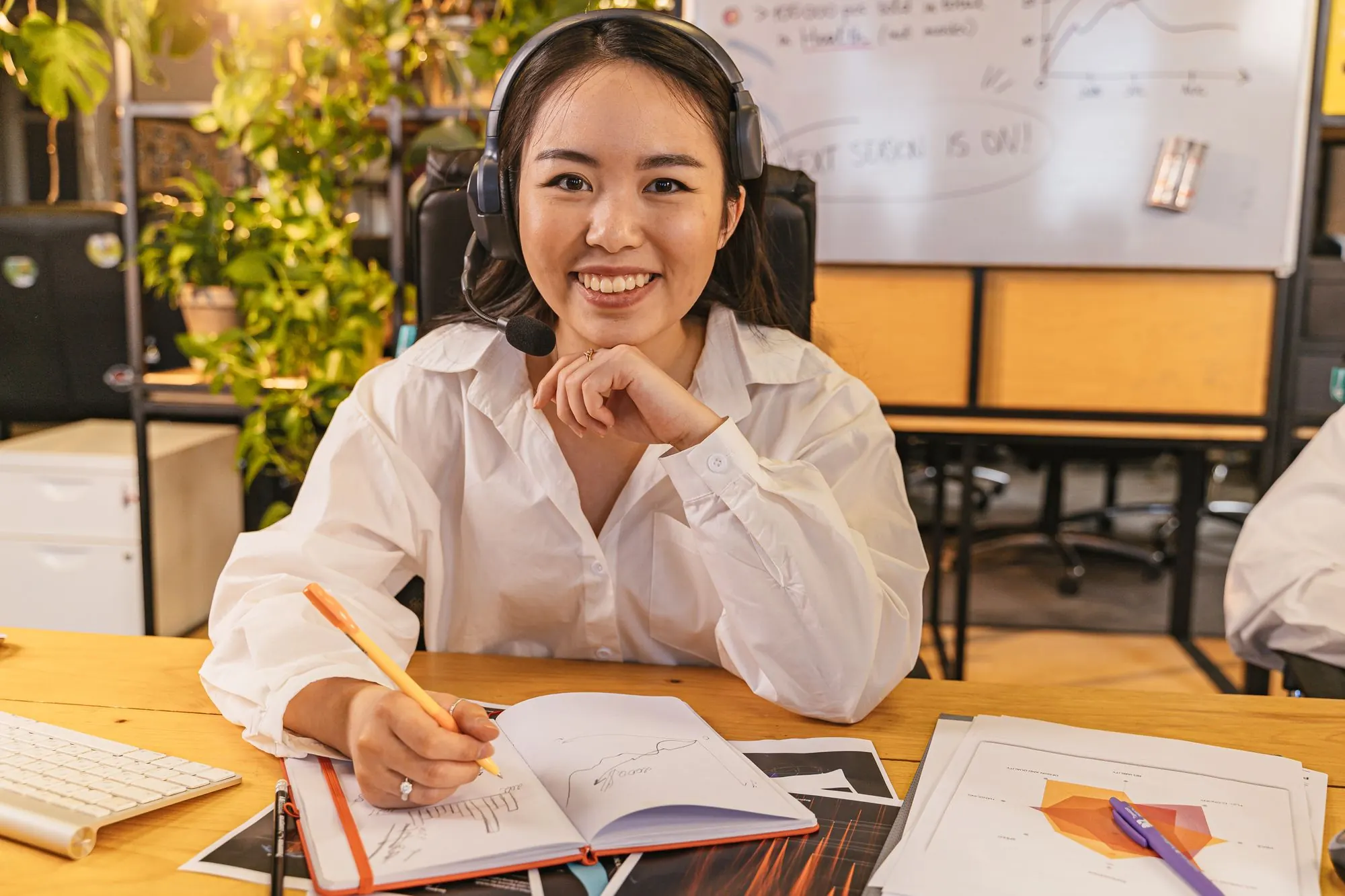 Smiling woman with a headset taking notes at a sunny desk