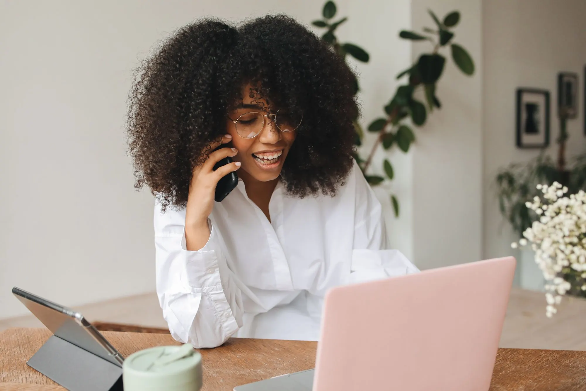 Smiling woman talking on her mobile phone at a desk with a laptop