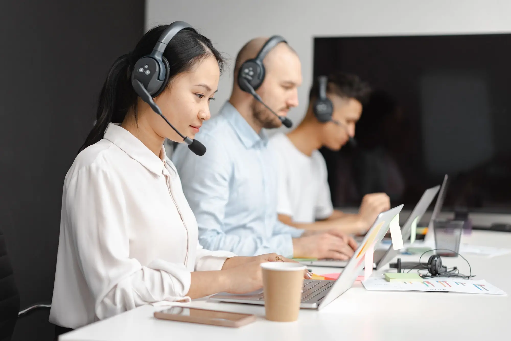 Sales team on headsets working at laptops side by side